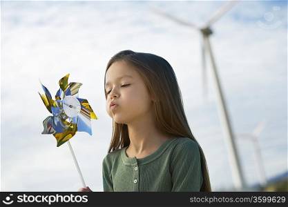 Girl (5-6) blowing toy windmill at wind farm