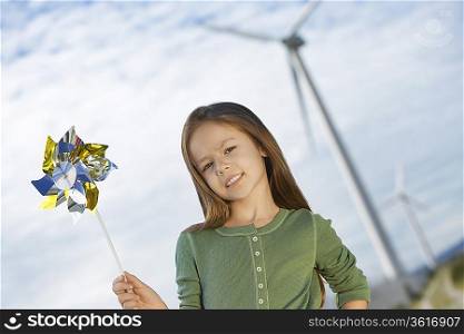 Girl (5-6) holding toy windmill at wind farm, portrait