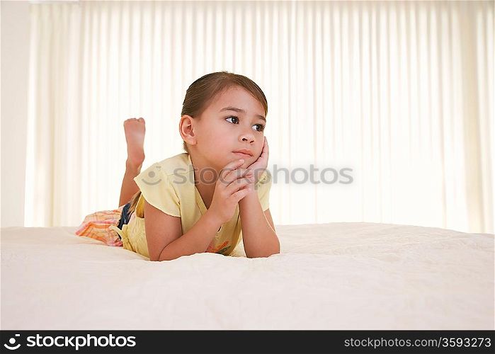 Girl (5-6) lying on bed looking away
