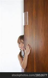Girl (5-6) peeking from behind door