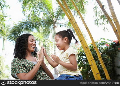 Girl (5-6 years) clapping hands with mother in forest low angle view
