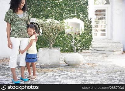 Girl (5-6 years) hugging mothers leg standing in yard