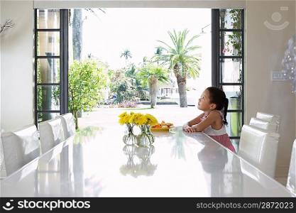 Girl (5-6 years) sitting at dining table side view