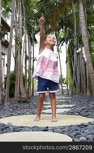 Girl (5-6 years) standing on stepping stone on path pointing up