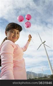 Girl (7-9) holding balloons at wind farm, portrait