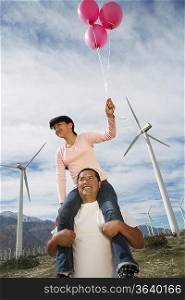 Girl (7-9) holding balloons, sitting on fathers shoulders at wind farm