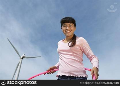 Girl (7-9) holding hula hoop at wind farm, portrait
