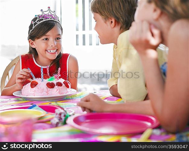 Girl (7-9) with birthday cake talking to guests at birthday party