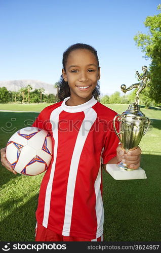 Girl (7-9 years) soccer player holding trophy and ball, portrait