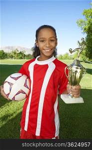 Girl (7-9 years) soccer player holding trophy and ball, portrait