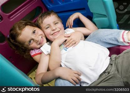 Girl and a boy sitting on a slide and smiling