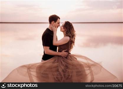 girl and a guy on the shore of a pink salt lake at sunset