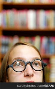 Girl and books. People: young girl, student, wearing eyeglasses, chooses a book in a library or bookstore, close-up portrait, intentional partial crop.