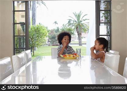 Girl and boy (5-6 years) eating at dining table