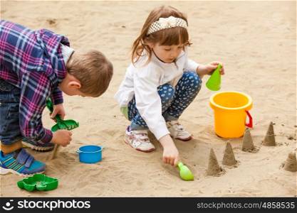Girl and boy building figures with sand in a sandbox. Children playing in a sandbox