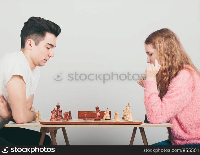 Girl and boy playing chess at home, they are concentrated on their next moves. Teenagers sitting by a table. Profile view. Copy space for text in the middle of image