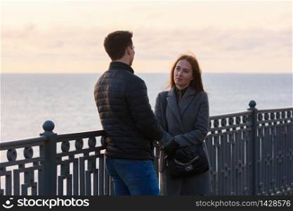 Girl anxiously looks at a guy near a railing in the background of the sea in cloudy weather