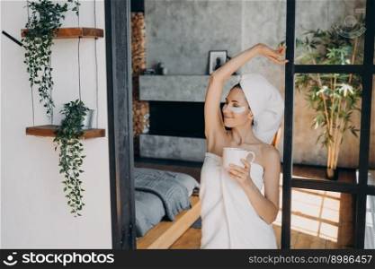 Girl applies anti age eye patches and smiling. Weekend morning at home. Young lady with cup of coffee relaxing at luxurious spa resort. Beautiful european woman wrapped in towel after bathing.. Girl applies anti age eye patches and smiling. Weekend morning at home or luxurious spa resort.