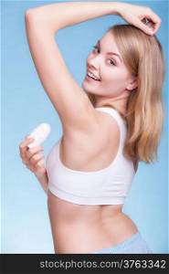 Girl applying stick deodorant in armpit. Young woman putting antiperspirant in underarms on blue. Daily skin and body care. Studio shot.