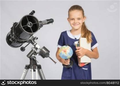 Girl astronomer is a telescope with a globe and books in the hands