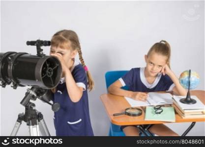 Girl astronomer looks at the sky through a telescope, the other girl is sitting at the table