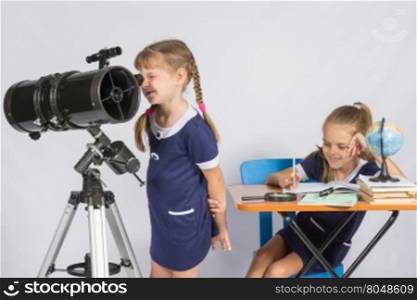 Girl astronomer looks through the eyepiece of the telescope, and the other girl sitting happily at the table