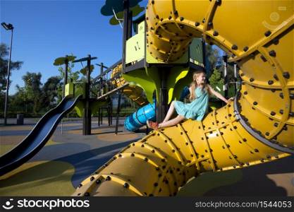 girl at the large beautiful playground in the park. Summer and active lifestyle