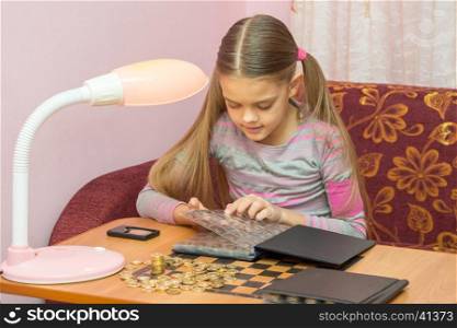 Girl at the table leafing through the album with coins