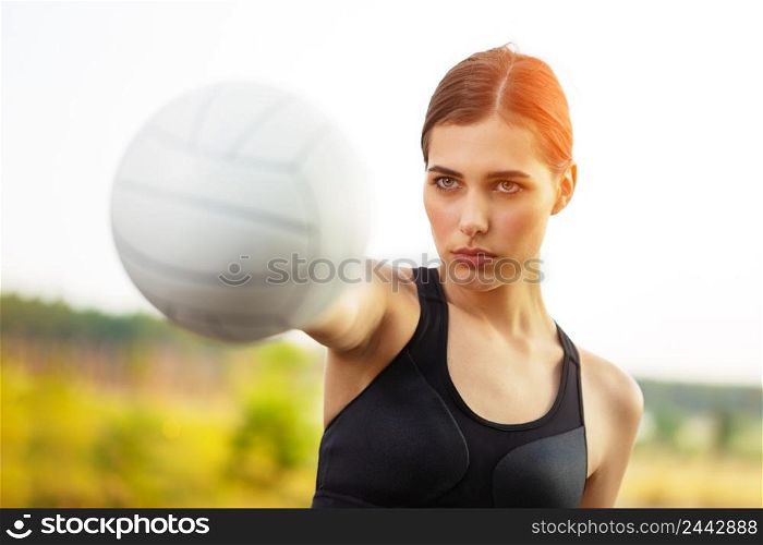 Girl athlete holding a white ball in an outstretched hand against the backdrop of a bright sun. Girl athlete holding white ball in outstretched hand against backdrop of bright sun