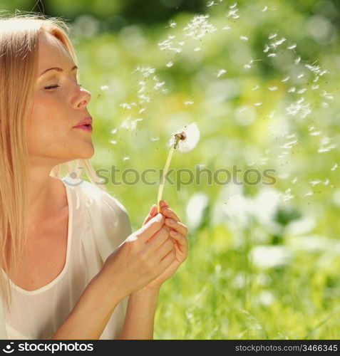 girl blowing on a dandelion lying on the grass