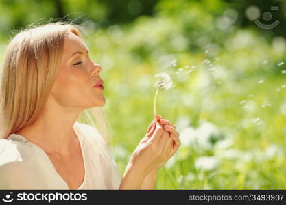 girl blowing on a dandelion lying on the grass