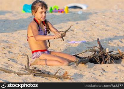 Girl breaks brushwood for a bonfire on a sandy beach