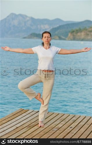 girl by holding a balance while standing on one leg on pier