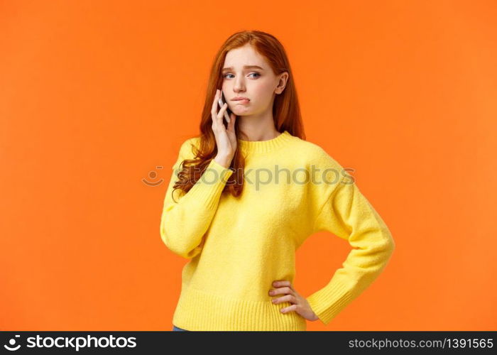 Girl catching anxiety calling someone. Perplexed or nervous cute redhead woman biting lip and looking away as having conversation on mobile phone, standing orange background sad.. Girl catching anxiety calling someone. Perplexed or nervous cute redhead woman biting lip and looking away as having conversation on mobile phone, standing orange background sad