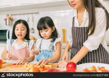 Girl child enjoy playing cut apple together with mother and sister at home kitchen.