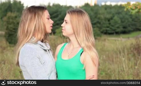Girl comforting her female friend with kiss and hug. Action on natural background.