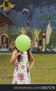 Girl covering her face with a balloon in a park