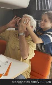 Girl covering her grandfather&acute;s eyes from behind