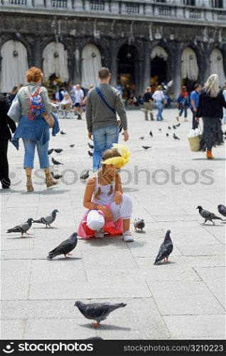 Girl crouching near pigeons, Venice, Veneto, Italy