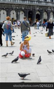 Girl crouching near pigeons, Venice, Veneto, Italy