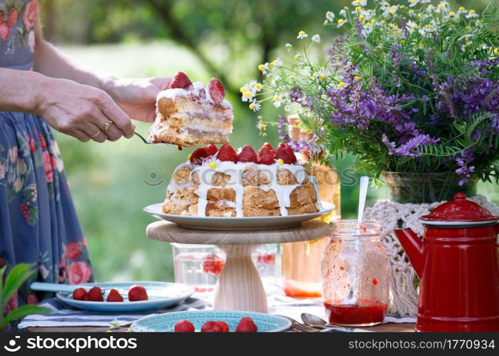 girl cuts biscuit with strawberries. dining table in the garden.