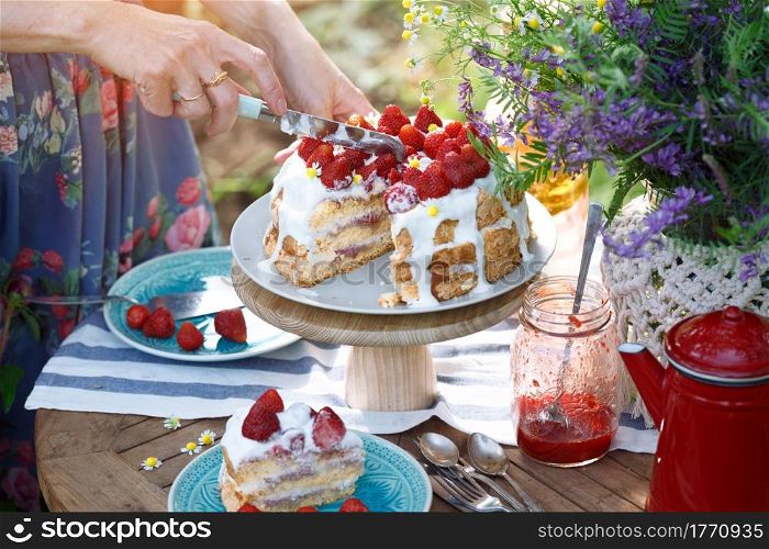 girl cuts biscuit with strawberries. dining table in the garden.