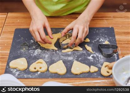 Girl cutting the dough to heart shapes for the cookies. Kid taking part in baking workshop. Baking classes for children, aspiring little chefs. Learning to cook. Combining and stirring prepared ingredients. Real people, authentic situations