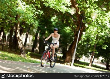 Girl cycling in the park. She’s wearing white sport clothes, cap, her bicycle is red. It’s a sunny summer day.