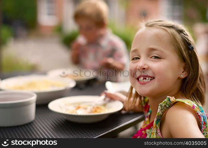 Girl dining at garden table, looking over shoulder smiling at camera