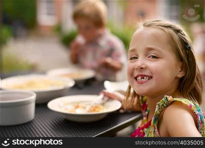 Girl dining at garden table, looking over shoulder smiling at camera