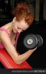 Girl doing biceps exercise with dumbbell in the gym