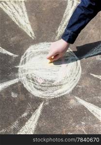 girl drawing a sun with colored chalk on pavement on street