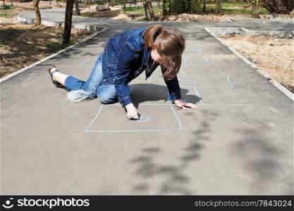 girl drawing hopscotch outdoors in sunny day