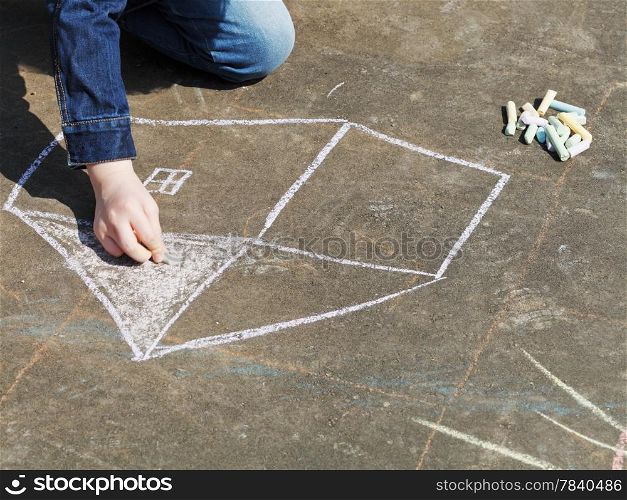girl drawing house with colored chalk on pavement on street